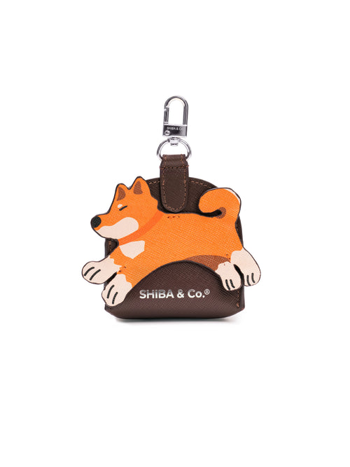 Brown Italian saffiano leather dog poop bag holder with a Shiba Inu illustration and gold clasp, clipped to a lead.
